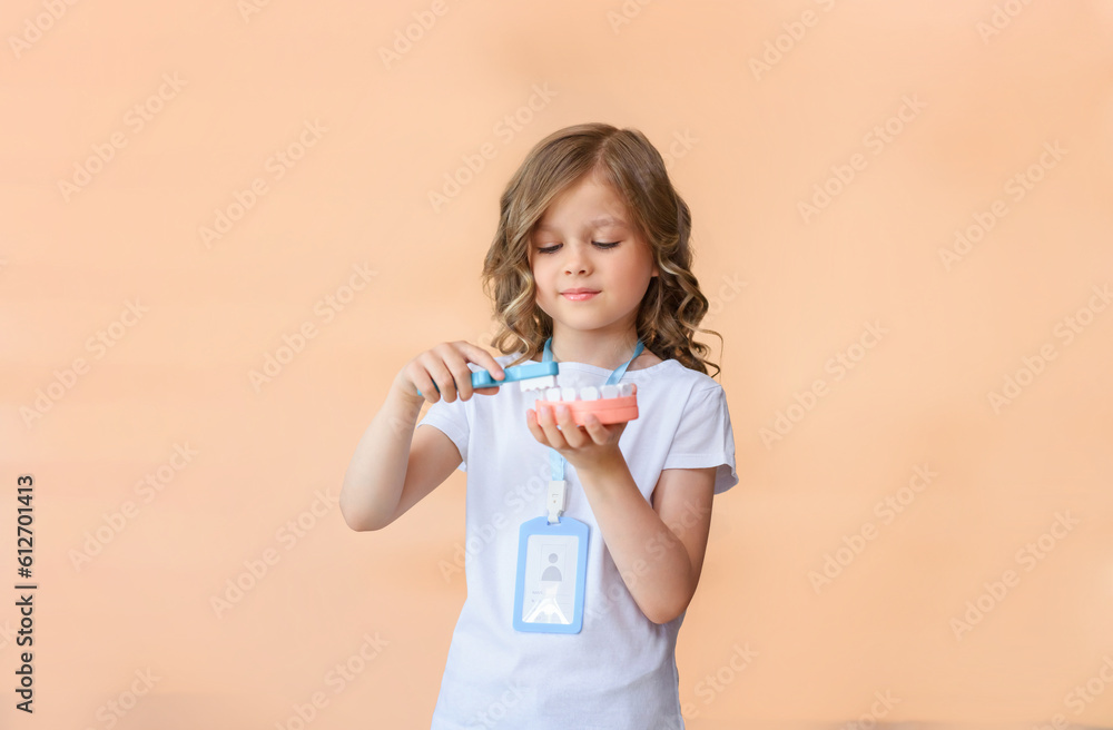 A little dentist girl holds a model of a human jaw and a toothbrush in her hands to demonstrate proper tooth brushing isolated on pink studio background. International Dentist's Day. copy space A little dentist girl holds a model of a human jaw and a toothbrush in her hands to demonstrate proper tooth brushing isolated on pink studio background. International Dentist's Day. copy space