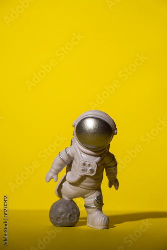 Plastic toy astronaut on colorful yellow background Copy space. Concept of out of earth travel, private spaceman commercial flights. Space missions and Sustainability
