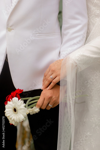 Bride and groom hands with engagement rings and bridal white red bouquet