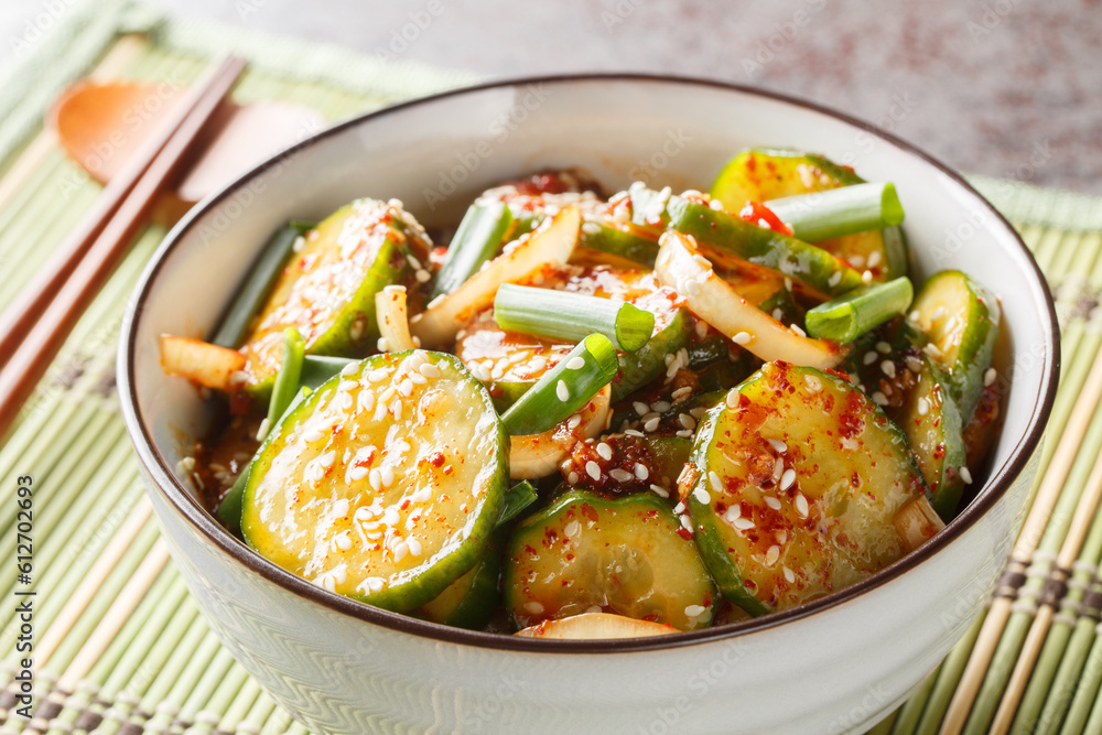 Spicy Korean cucumber salad in kimchi sauce with sesame seeds in a bowl with chopsticks on the table. Horizontal Spicy Korean cucumber salad in kimchi sauce with sesame seeds in a bowl with chopsticks on the table. Horizontal
