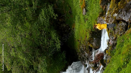 Gudvangen-Naeroyfjorden, Norway. Vertical Footage Video. Waterfall Tuftofossen In Spring. Young Caucasian Woman Lady Tourist Traveler Photographer Hands Up Enjoying Life. photo