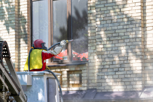 Fotografie A worker in a protective space suit cleans the facade of an old brick house using an industrial sandblaster