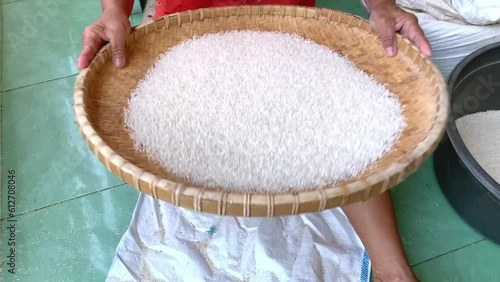 close up of a hand of a person winnowing rice on a round rattan tray. photo