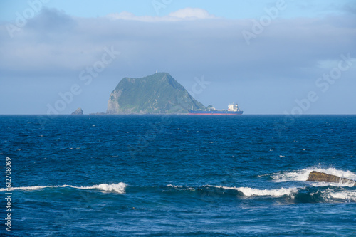 A freighter is about to pass a small island in the sea. View of Keelung Harbor from Wanli Beach in New Taipei City. Taiwan. photo