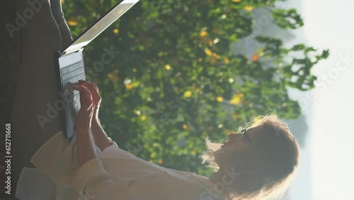 Wallpaper Mural Vertical shot of blonde woman typing on a laptop keyboard in sunshine outdoor. Female writer working on the rooftop with a beautiful view at sunrise. Torontodigital.ca