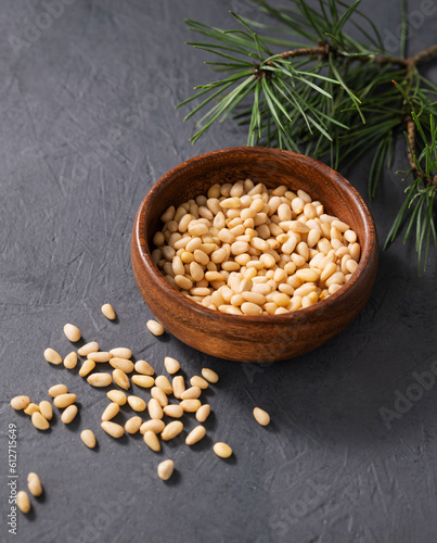 Pine nuts in a wooden bowl and scattered on a dark background with branches of pine needles close up. The concept of a natural, organic and healthy superfood and snack.
