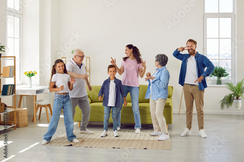 Big friendly family grandparents, parents and children dancing in living room at home. They are happy having fun spending time together on weekend. Three generations, lovely family moments concept.