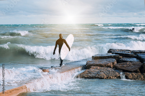 Male surfer carrying a surfboard and walking into the sea