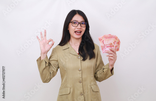 Wow delighted young Asian teacher holding Indonesian banknotes while showing okay hand gesture photo