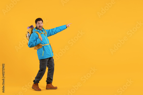 Emotional man with backpack pointing at something on orange background, space for text. Active tourism
