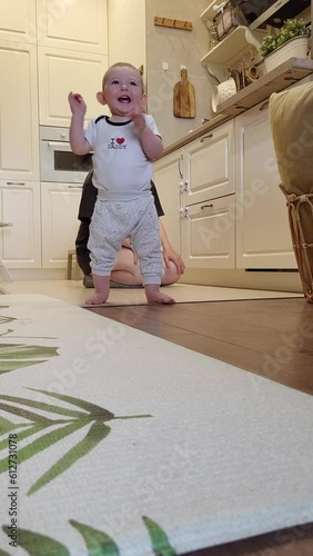 Toddler baby boy learns to walk holding on to his mother. Kid aged about one year (eleven months)