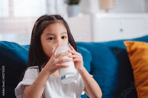 Cute Asian girl drinking milk at home to nutrition vitamin healthy and strong teeth.