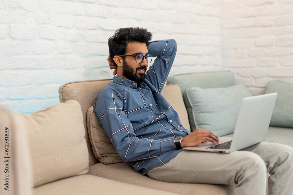 Brunette bearded young man with a laptoop sitting on the sofa