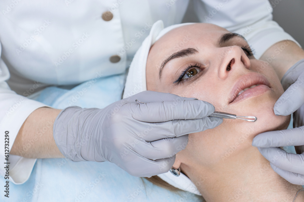 A dermatologist examines the skin of a young woman's face under a lamp A dermatologist examines the skin of a young woman's face under a lamp
