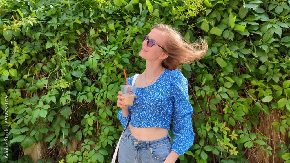Beautiful woman in blue blouse in green park smiling drinking iced coffee and enjoying summer sunshine. Coffee break on work. Slow motion 4k footage. Beautiful woman in blue blouse in green park smiling drinking iced coffee and enjoying summer sunshine. Coffee break on work. Slow motion 4k footage.