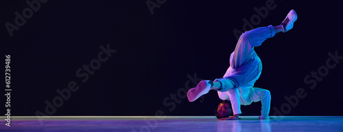 Young active man in casual clothes dancing hip-hop, breakdance against black studio background in neon light