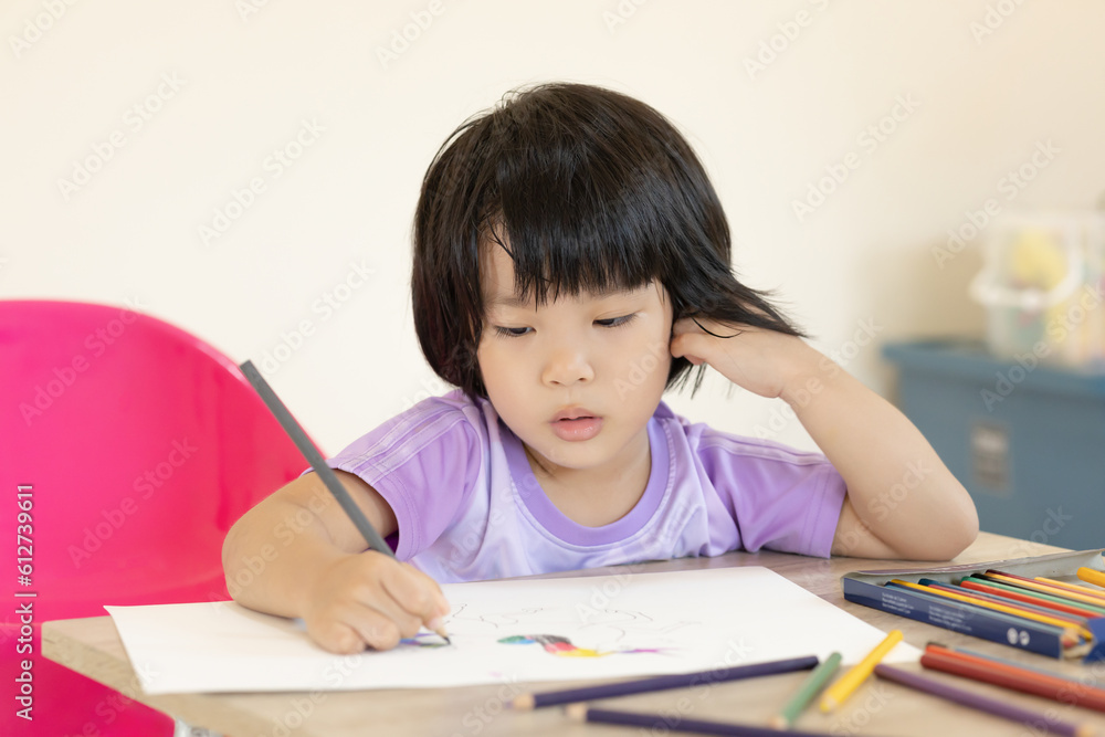 Cute girl is learning letters at home. Adorable girl Children paint on white paper. The coloring book is placed on brown wooden table. Child are happy to make art. Cute girl is learning letters at home. Adorable girl Children paint on white paper. The coloring book is placed on brown wooden table. Child are happy to make art.