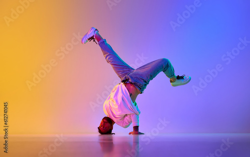 Creative young guy in casual clothes dancing hip-hop contemporary, breakdance against gradient studio background in neon light