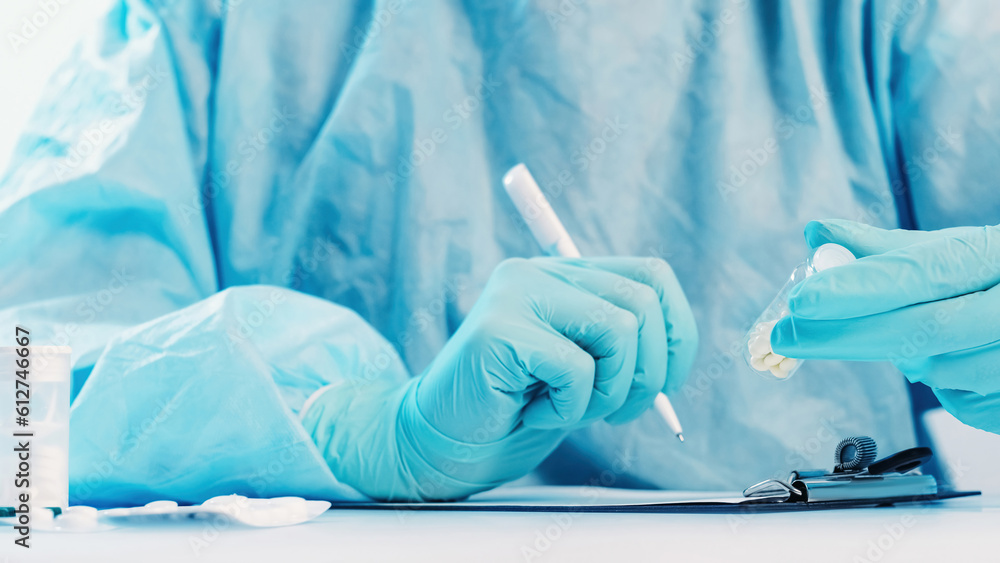 Fototapeta premium Antibiotic prescription. Medical advice. Doctor hands in blue protective gloves with pills bottle writing drug dosage on clipboard with tablets blisters on white table.