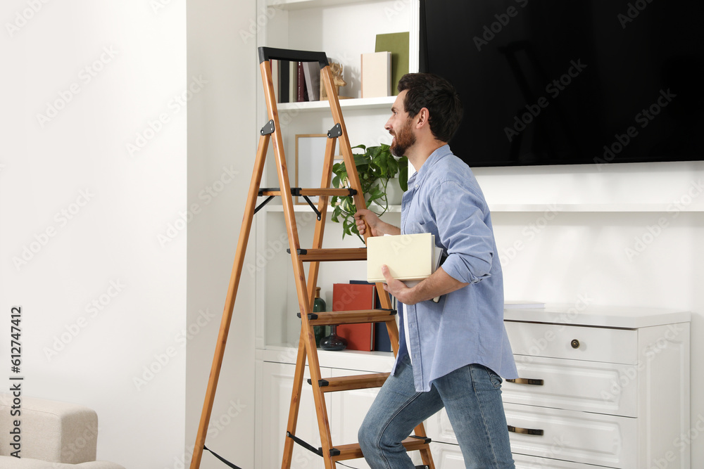 Man with books on wooden folding ladder at home
