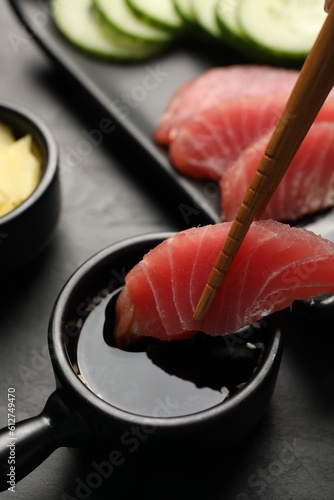 Dipping tasty sashimi (piece of fresh raw tuna) into soy sauce at black table, closeup