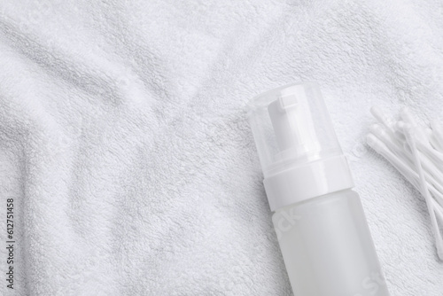 Bottle of face cleansing product and cotton buds on white towel, flat lay. Space for text