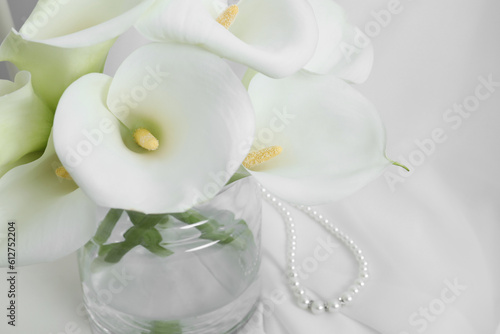 Beautiful calla lily flowers in glass vase on white cloth, closeup