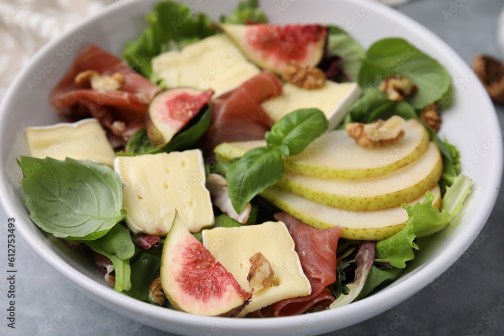 Tasty salad with brie cheese, prosciutto, pear and figs on grey table, closeup