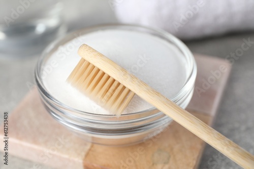Bamboo toothbrush and glass bowl of baking soda on light table, closeup