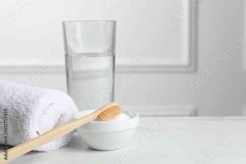 Bamboo toothbrush  bowl of baking soda  towel and glass of water on white table. Space for text