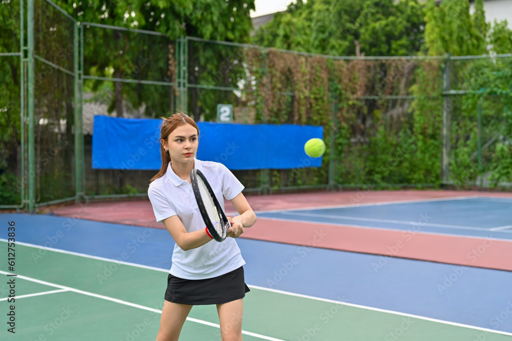 Pretty young woman hitting ball with racket to return ball over net. Sport, fitness, training and active life concept