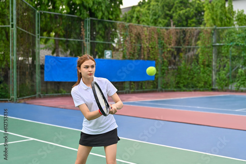 Pretty young woman hitting ball with racket to return ball over net. Sport, fitness, training and active life concept © Prathankarnpap