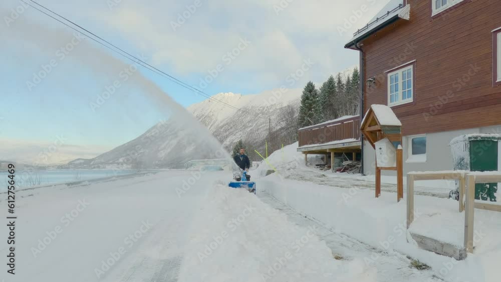 Male removing hard compact snow with snow blower on a cold sunny winter day with a scenic landscape Male removing hard compact snow with snow blower on a cold sunny winter day with a scenic landscape