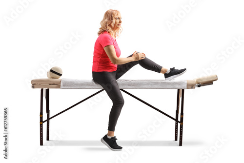 Mature woman in a sportswear sitting on a therapy table and holding her knee