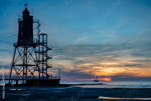 Obereversand lighthouse and the fishing cutter on the open seascape at sunset. Silhouette of the historic lighthouse Obereversand in Am Kutterhafen, Dorum-Neufeld, Wurster Nordseekuste, Germany.  photo