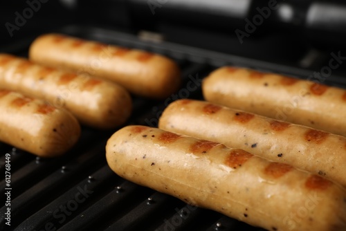 Delicious vegan sausages cooking on electric grill, closeup