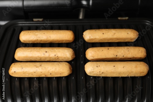Delicious vegan sausages cooking on electric grill, closeup