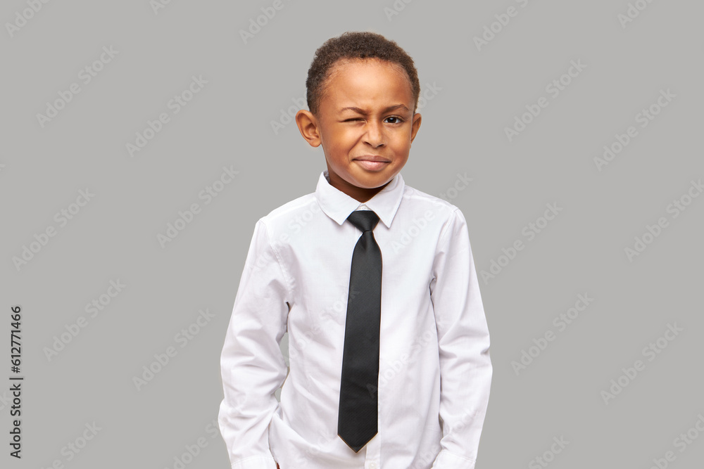 Studio shot of happy schoolboy of african ethnicity winking at camera being in perfect mood at first day at school, dressed in uniform, wearing white shirt and black necktie. Children and formal wear Studio shot of happy schoolboy of african ethnicity winking at camera being in perfect mood at first day at school, dressed in uniform, wearing white shirt and black necktie. Children and formal wear