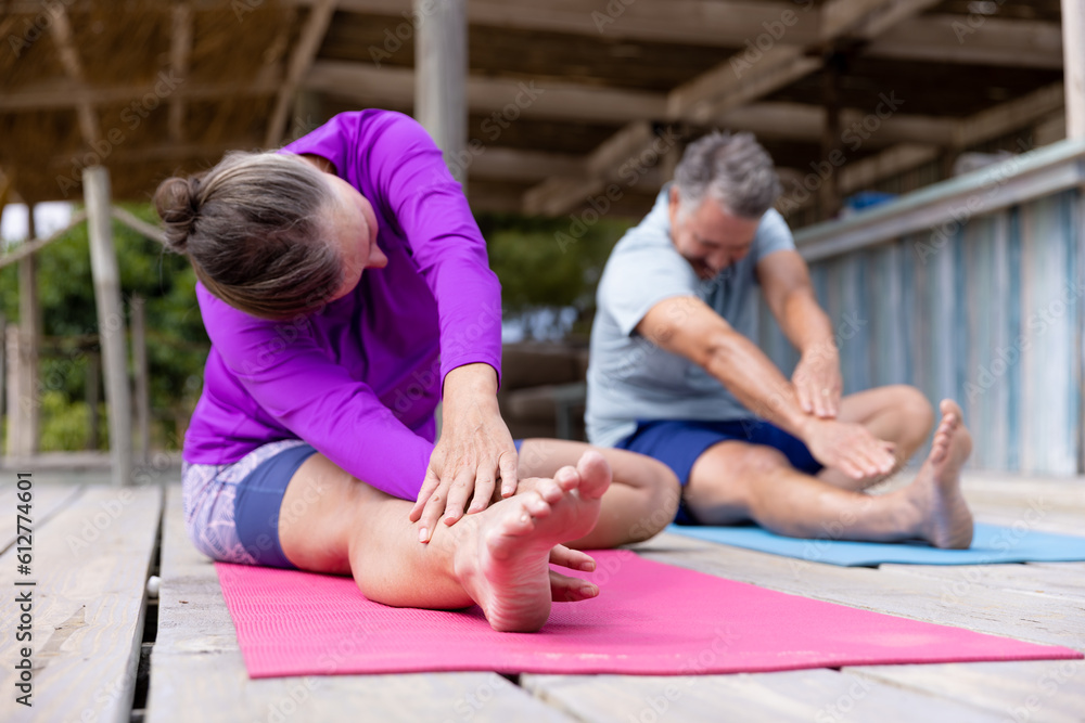 Caucasian senior couple stretching hands and legs while practicing yoga on floor at tourist resort