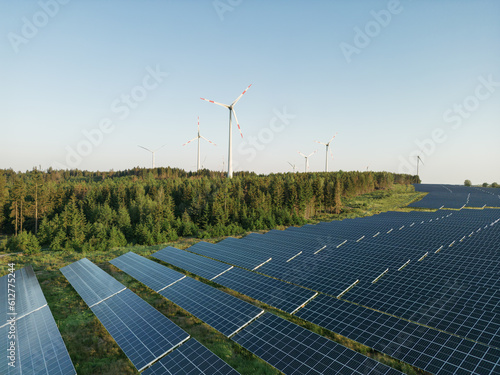 Photovoltaik-Anlage in grüner Landschaft mit Windrädern im Hintergrund bei Sonnenschein