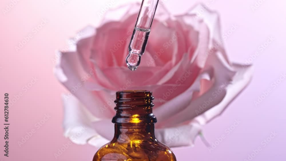 Rose essential oil falling from glass dropper into a cosmetic bottle