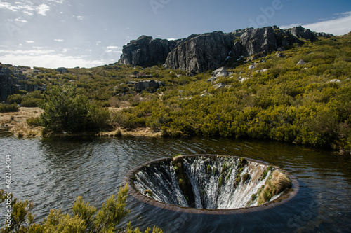 Discover the mesmerizing Covão dos Conchos, a captivating lake with a distinctive hole, nestled in Serra da Estrela, Portugal. Majestic rocks and lush bushes frame this enchanting natural wonder. photo