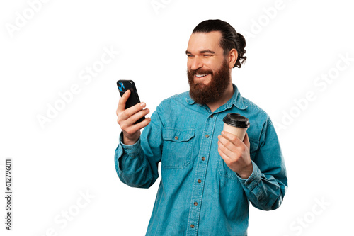 Laughing bearded man enjoys the coffee break while browsing his phone.