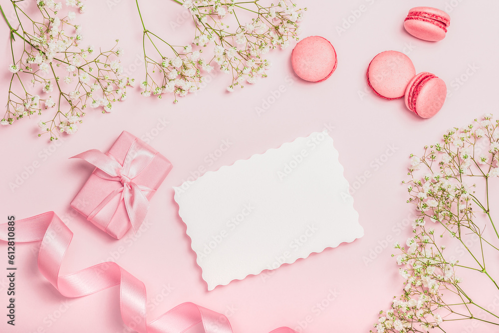 Flat lay composition with empty blank, macaroon, gift box, satin ribbon and gypsophila on pink background. Stylish women's workplace. Greeting card