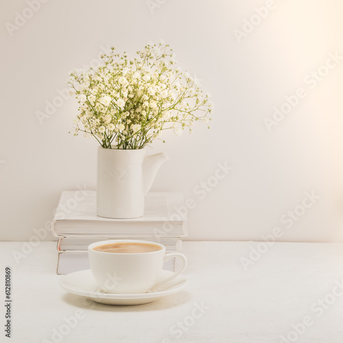 Coffee  a bouquet of gypsophila and a stack of books on a white table. Cozy breakfast.