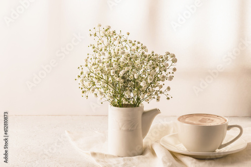 Coffee, a bouquet of gypsophila in a white vase on a white table. Cozy breakfast. photo