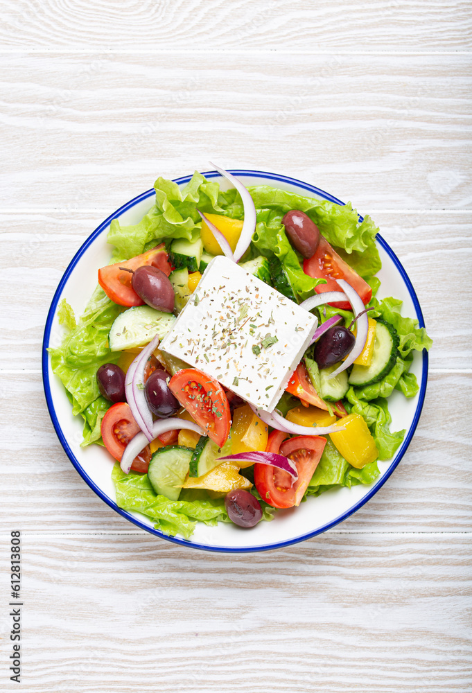 Traditional Greek Salad with Feta Cheese, Tomatoes, Bell Pepper, Cucumbers, Olives, Herbs in white ceramic bowl on White rustic wooden table background from above, Cuisine of Greece Traditional Greek Salad with Feta Cheese, Tomatoes, Bell Pepper, Cucumbers, Olives, Herbs in white ceramic bowl on White rustic wooden table background from above, Cuisine of Greece