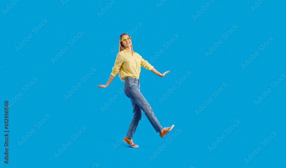 Overjoyed funny millennial teenager girl isolated on blue studio background dancing. Smiling young woman in glasses and casual wear have fun make dancer moves. Entertainment concept.