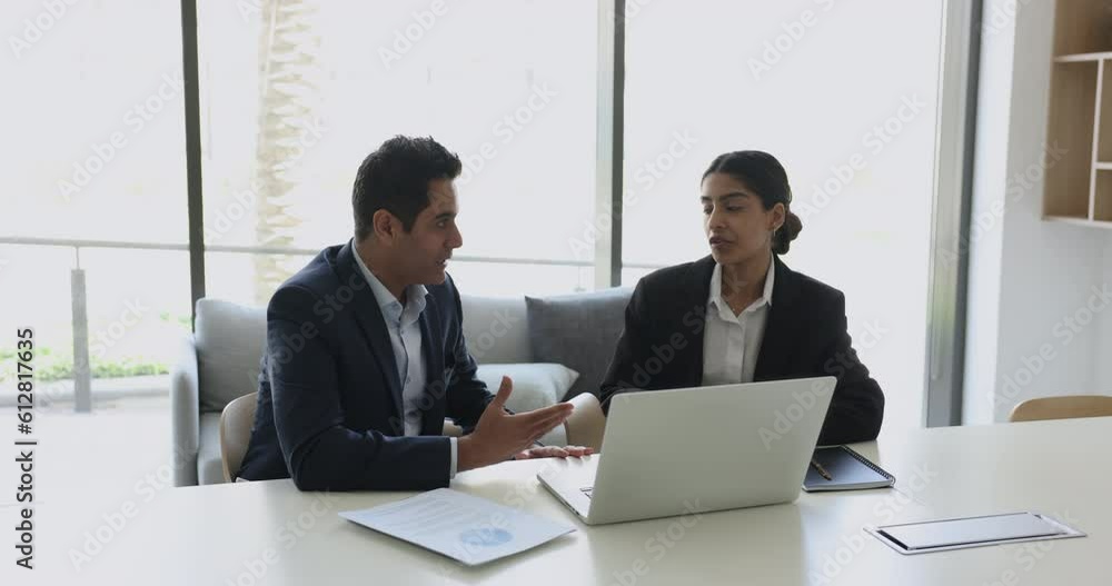 Two serious indian business partners sit at desk in boardroom, share ideas, working on project together with laptop, makes business proposal, explain deal detail, prepare joint plan, analyzes result Two serious indian business partners sit at desk in boardroom, share ideas, working on project together with laptop, makes business proposal, explain deal detail, prepare joint plan, analyzes result