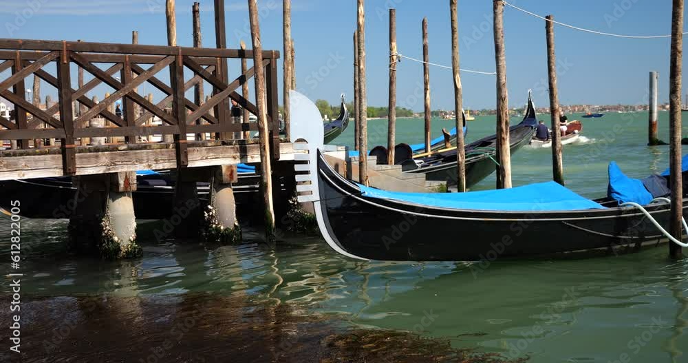 Gondola moored with palines at the ferry pier near the waterfront at the Riva degli Schiavoni, in Venice, Italy. Gondola moored with palines at the ferry pier near the waterfront at the Riva degli Schiavoni, in Venice, Italy.